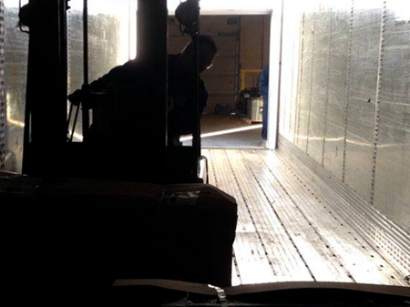 Silhouette of forklift, and driver, loading spent lead acid batteries onto truck.